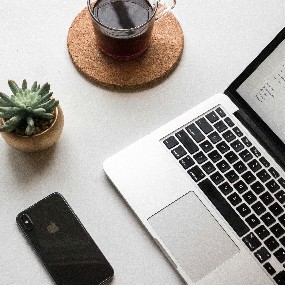 Image of a laptop, mobile phone and hot drink on a desk.